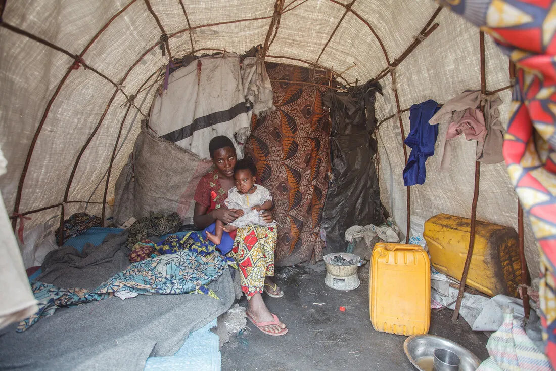 A mother sitting inside her makeshift shelter with one of her children.
