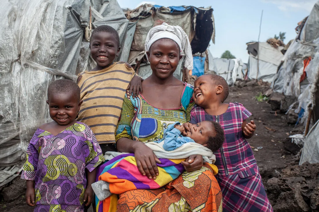 A woman sits in front of a makeshift shelter with four children, likely her own.