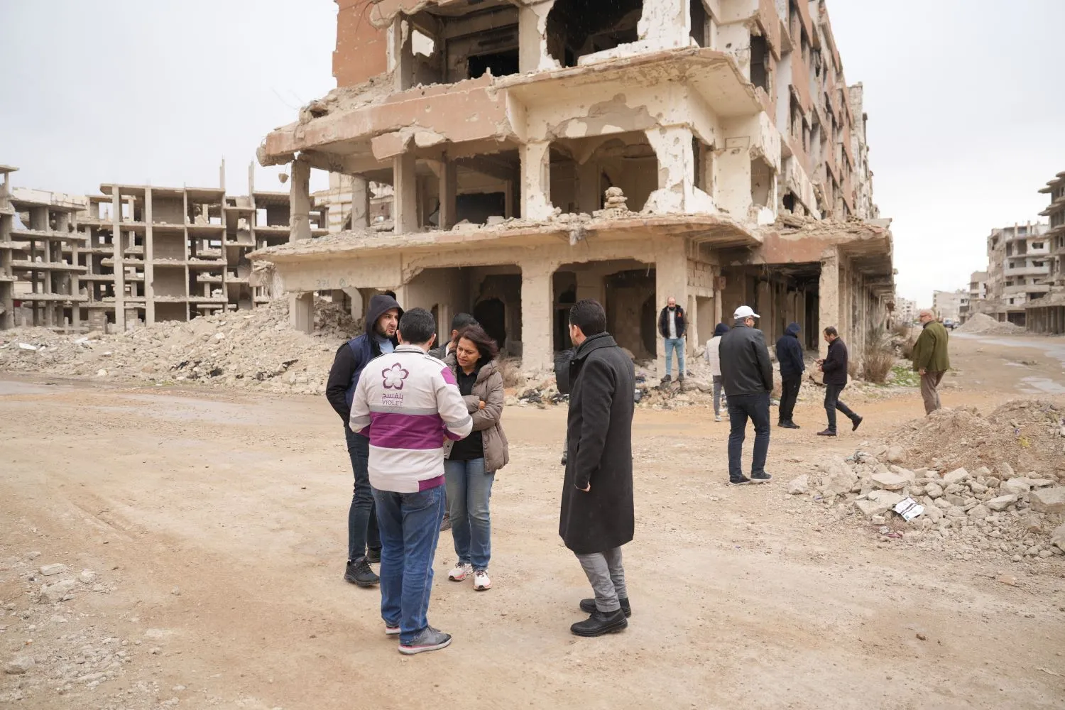 A group of humanitarian workers talking with each other in front of damaged buildings in a disaster zone.