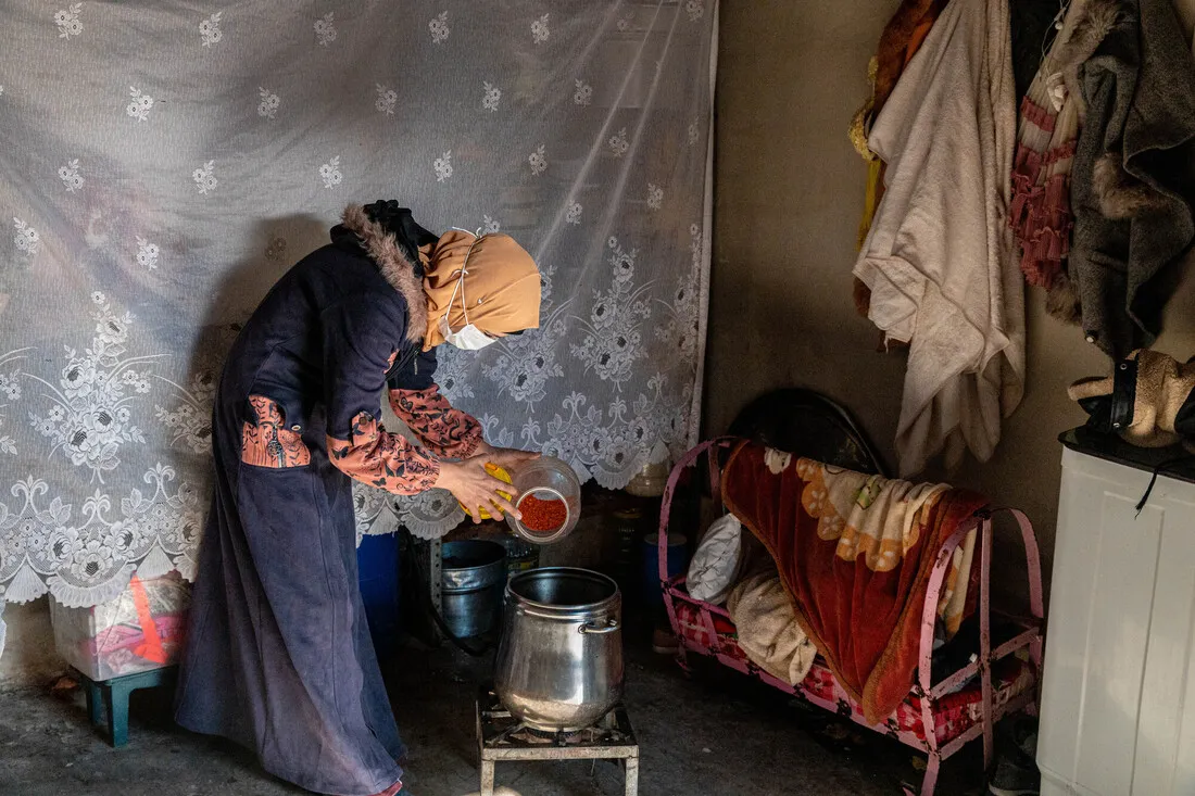 A woman fully covered in traditional clothing cooks a meal inside a temporary shelter.