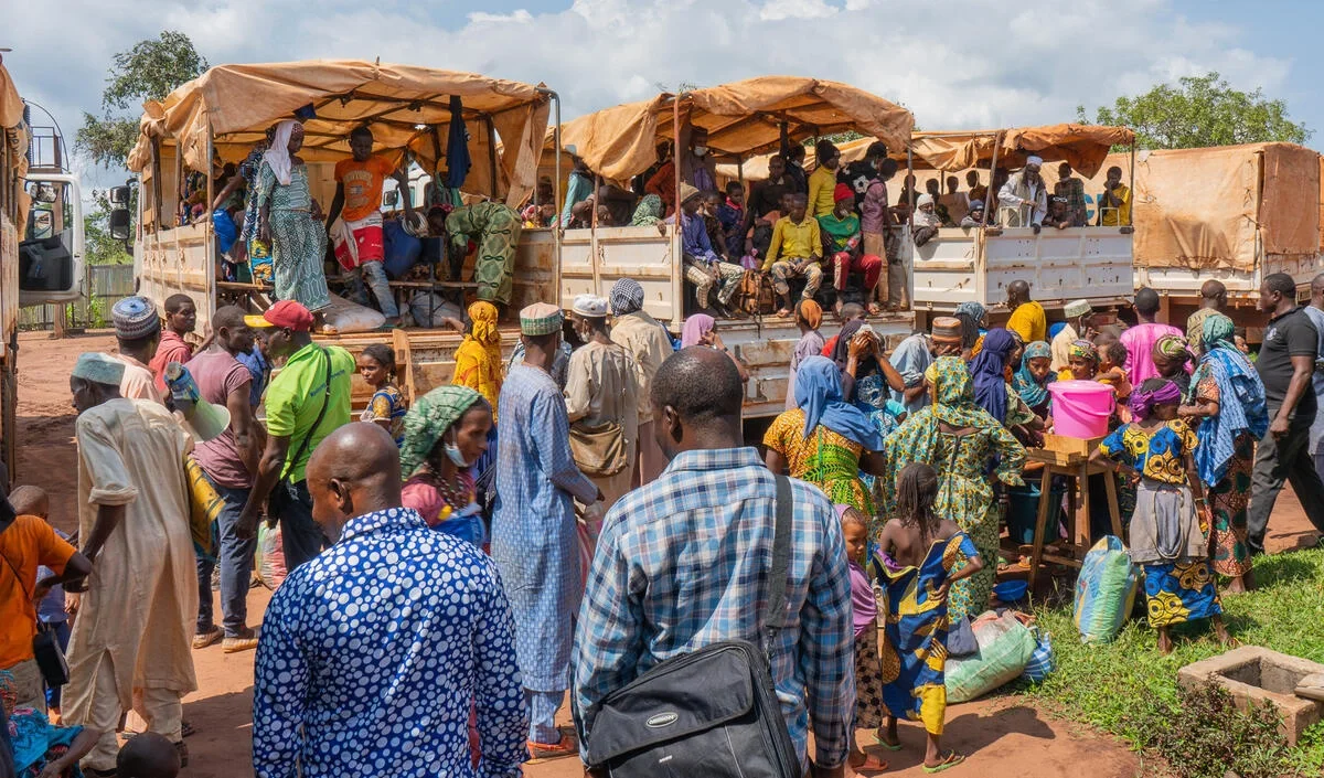 A group of people, including women and men, await their turn to receive essential supplies from aid trucks.