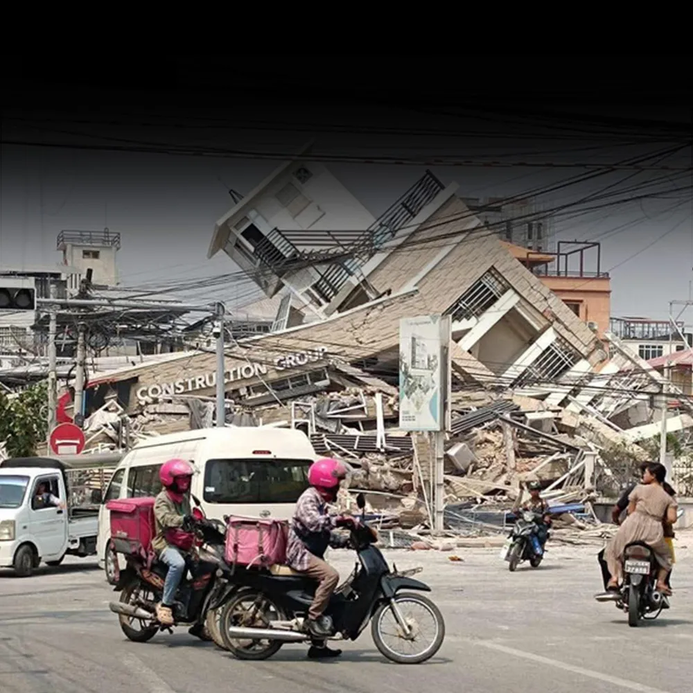 A few people riding motorbikes stop in the middle of the street to look at a building that has fallen down.