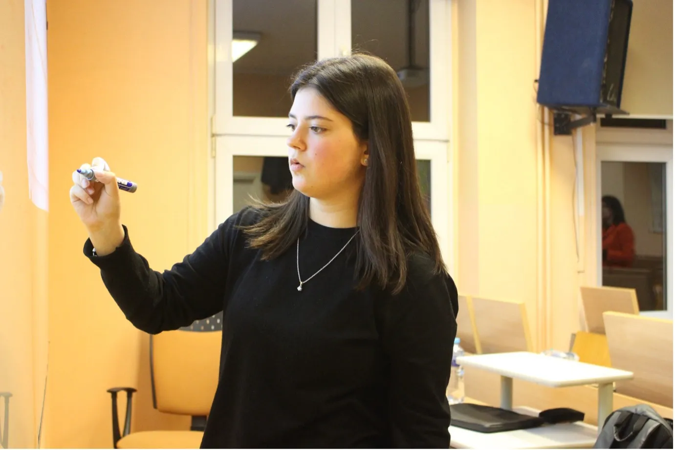 A young woman wearing a black shirt and looking to the left while holding a marker in her right hand.