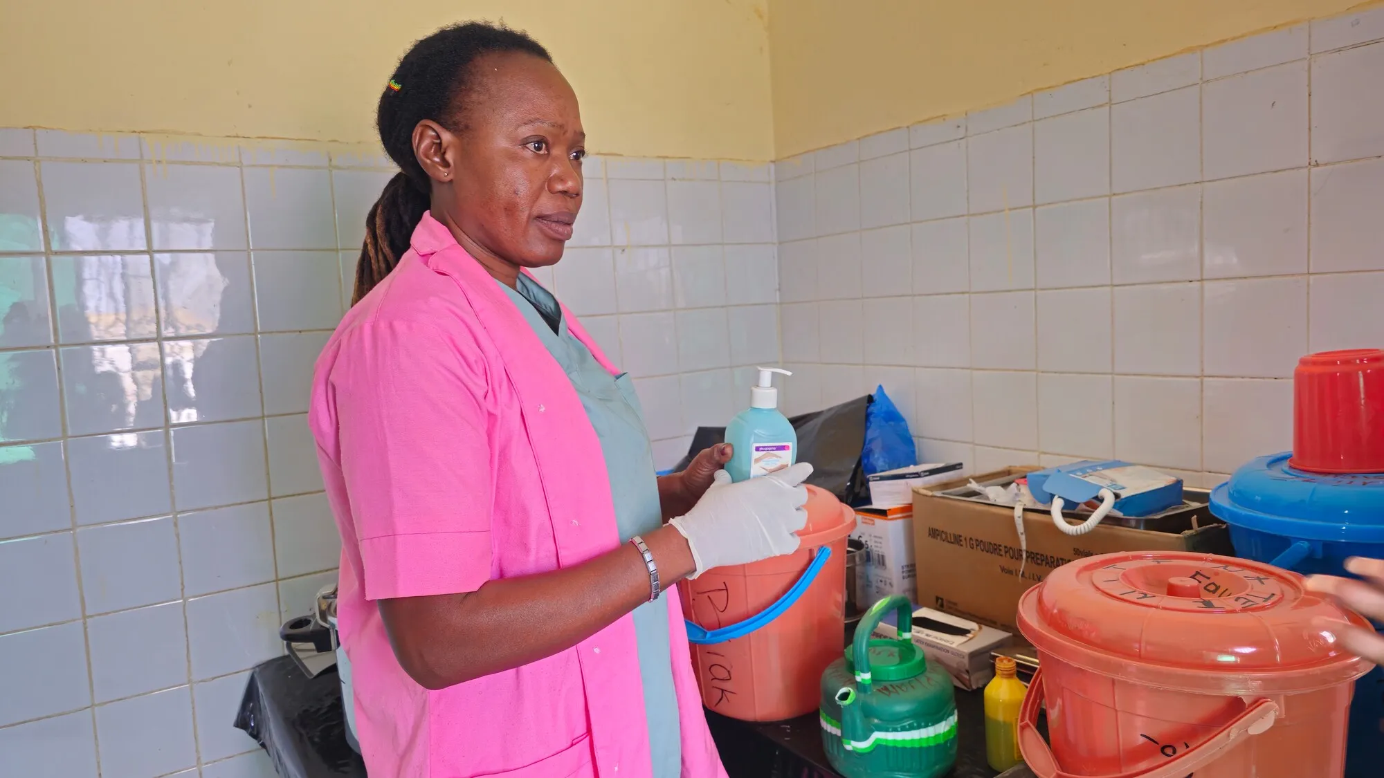 A woman in pink scrubs holds a bottle of hand sanitizer and looks at the supplies in a CARE-supported clinic in Chad.