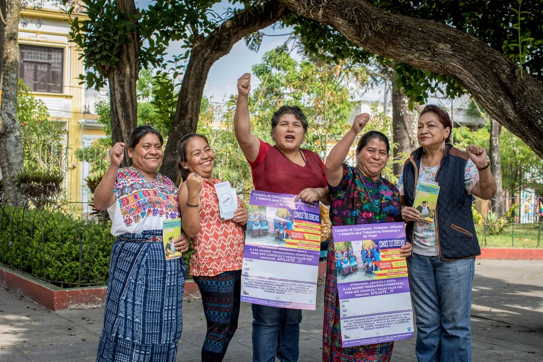 A group of women hold up flyers and cheer with their hands raised in the air.