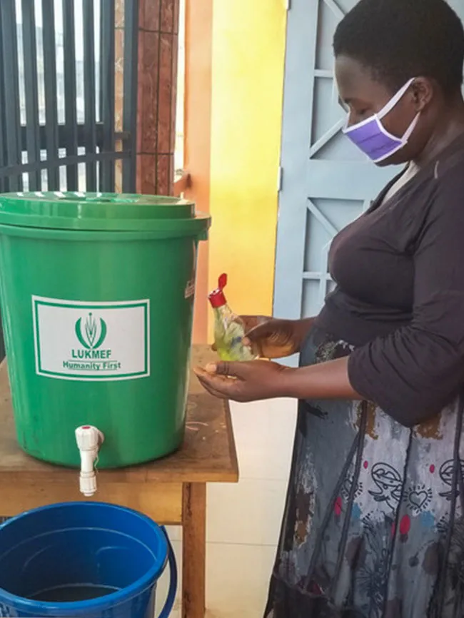 A woman washes her hands at a green washing station.