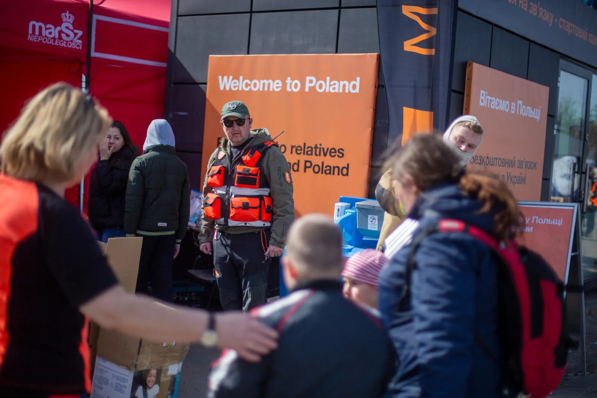 A man in a bright orange vest stands by an orange sign that reads, 