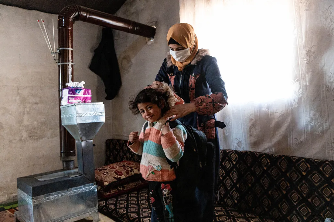 A mother in hijab and face mask prepares her child to go outside in a makeshift refugee camp hosting internally displaced people in Syria.